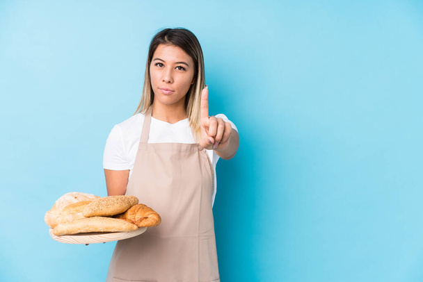 jonge Kaukasische bakker vrouw geïsoleerd tonen nummer een met vinger. - Foto, afbeelding