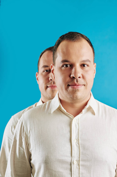 Young adult Caucasian man wearing white shirt standing behind his twin brother looking at camera, conceptual shot - Zdjęcie, obraz