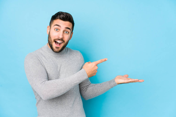 Young caucasian man against a blue background isolated excited holding a copy space on palm. - Foto, Imagem