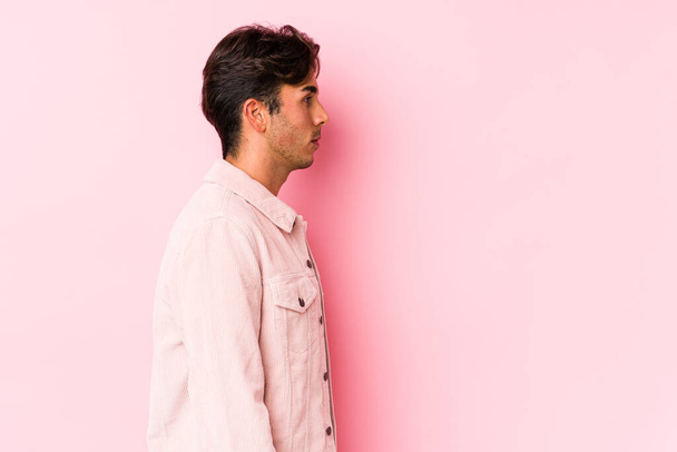 Νεαρός καυκάσιος άντρας ποζάρει σε ροζ φόντο απομονωμένος ατενίζοντας αριστερά, με πλάγια στάση.. - Φωτογραφία, εικόνα