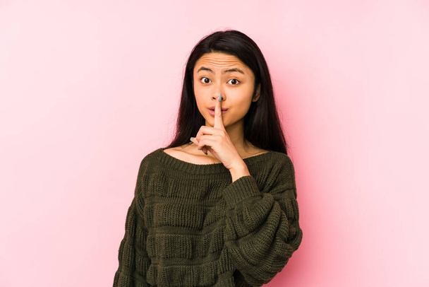 Junge Chinesin isoliert auf rosa Hintergrund hält ein Geheimnis oder bittet um Schweigen. - Foto, Bild