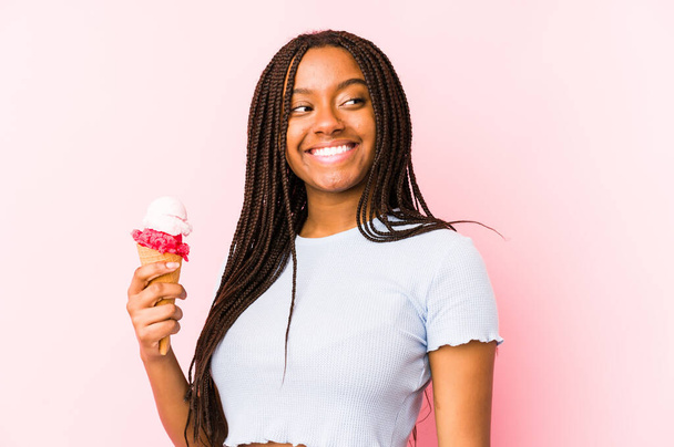 Jeune femme afro-américaine tenant une crème glacée isolée regarde de côté souriant, gai et agréable
. - Photo, image