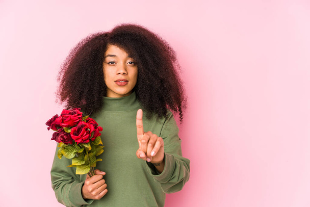 Jovem afro mulher segurando uma rosa isolada Jovem afro mulher segurando um rosesshowing número um com o dedo
. - Foto, Imagem