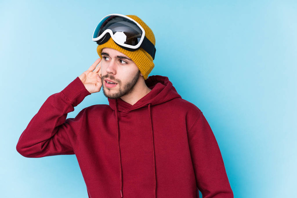 Jovem caucasiano vestindo uma roupa de esqui isolado tentando ouvir uma fofoca
. - Foto, Imagem