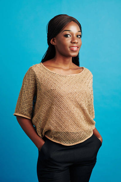 Mavi duvara yaslanmış gülümseyen güzel Afrikalı Amerikalı kadının dikey orta boy stüdyo portresi. - Fotoğraf, Görsel