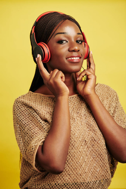 Вертикальная талия до студийного портрета красивой молодой чернокожей женщины, слушающей музыку с помощью наушников
 - Фото, изображение