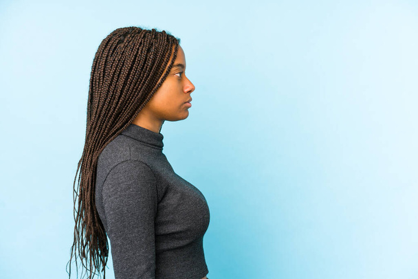 Mujer afroamericana joven aislada sobre fondo azul mirando a la izquierda, de lado posan. - Foto, Imagen