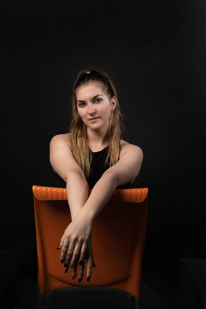 Girl sitting on an orange chair on a black background with cursivas appearance - Foto, immagini