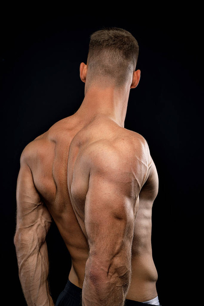 powerful muscular athlete shows off his back beside black wall - Fotó, kép