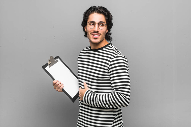 Mladý zaměstnanec, který drží soupis, se usmívá, je veselý a příjemný. - Fotografie, Obrázek