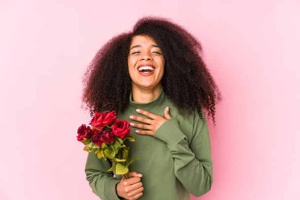 Молодая афро-женщина, держащая в руках розы, молодая афро-женщина, держа в руках розовый смех, громко держит руку на груди.
. - Фото, изображение