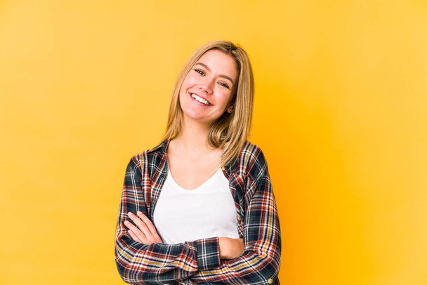 Young blonde caucasian woman isolated on yellow background who feels confident, crossing arms with determination. - Photo, Image