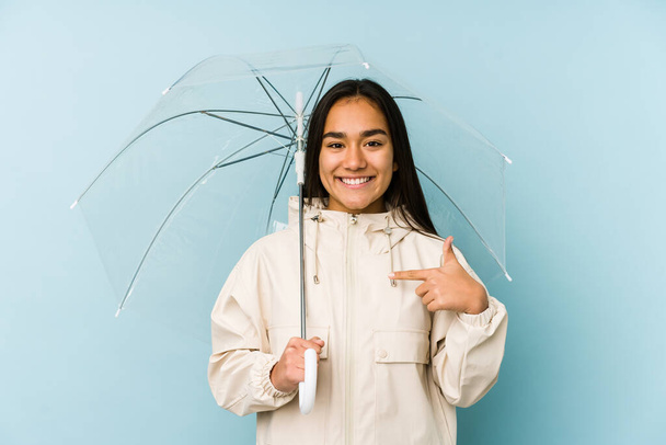 Young asian woman holding a umbrella person pointing by hand to a shirt copy space, proud and confident - Фото, зображення