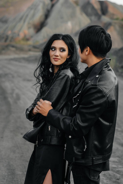 An Asian couple in love in black leather clothes walk in nature among the trees. Style, fashion, love - Photo, image