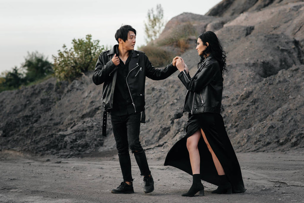 An Asian couple in love in black leather clothes walk in nature among the trees. Style, fashion, love - Foto, imagen