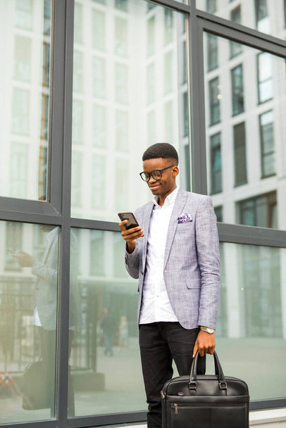 handsome young african man in a suit with a phone in his hands near a glass building - Zdjęcie, obraz