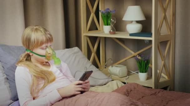 The child does inhalation at home, uses a smartphone. Boring and bad to get sick - Materiał filmowy, wideo
