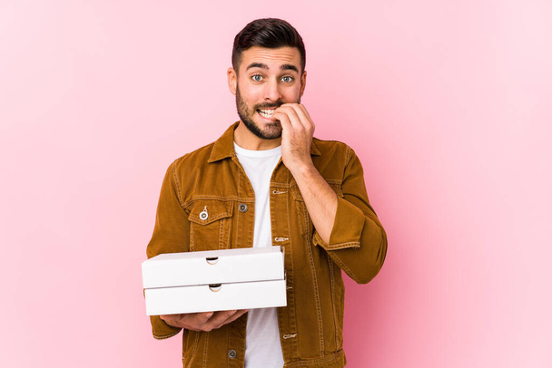 Mladý pohledný muž drží pizzy izolované kousání nehty, nervózní a velmi úzkostlivý. - Fotografie, Obrázek