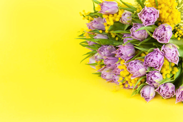 Bouquet of lilac tulips and yellow mimosas on yellow background, copy space, side view, closeup. March 8, February 14, birthday, Valentines, Mothers, Womens day celebration, spring concept - Photo, image