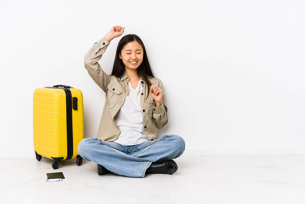 Joven viajera china sentada sosteniendo una tarjeta de embarque celebrando un día especial, salta y levanta los brazos con energía
. - Foto, imagen