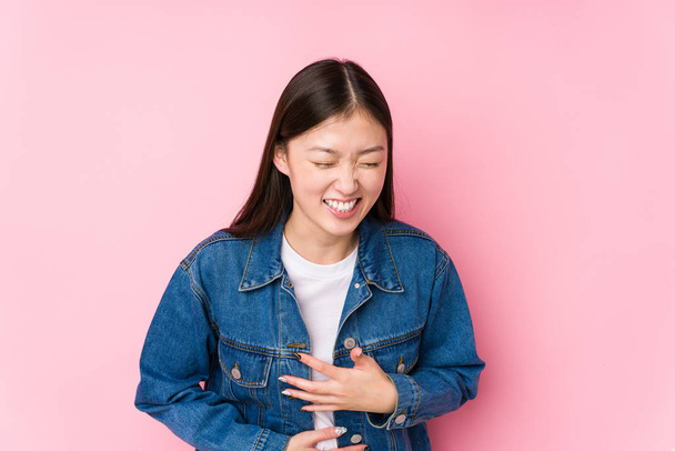 Young chinese woman posing in a pink background isolated laughs happily and has fun keeping hands on stomach. - Foto, imagen