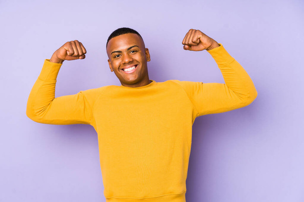 Young latin man isolated on purple background showing strength gesture with arms, symbol of feminine power - Photo, image