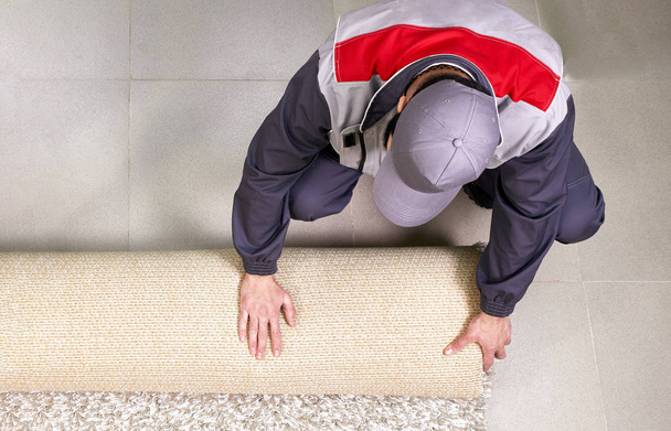 mężczyzna pracownik rozwijanie dywan na podłodze w domu, widok z góry - Zdjęcie, obraz