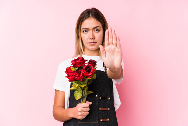 Νεαρή καυκάσιος γυναίκα κρατώντας ένα τριαντάφυλλα απομονωμένη στέκεται με απλωμένο το χέρι δείχνει στοπ, εμποδίζοντας σας. - Φωτογραφία, εικόνα