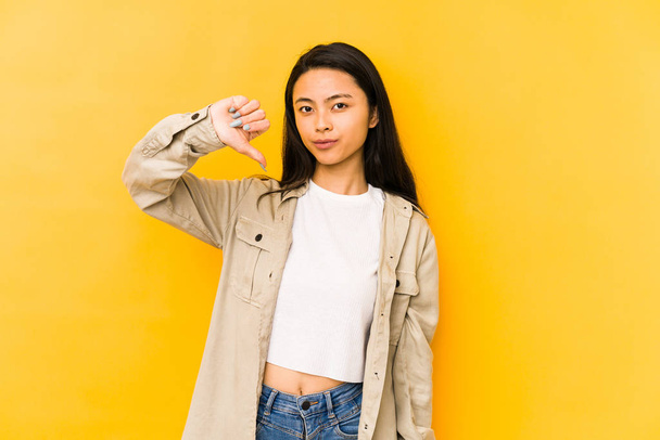 Young chinese woman isolated on a yellow background showing a dislike gesture, thumbs down. Disagreement concept. - Foto, imagen