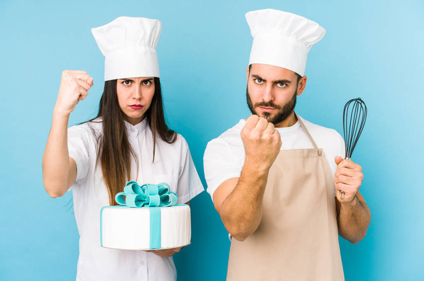 Junges Paar kocht gemeinsam einen Kuchen und zeigt vor laufender Kamera die Faust, aggressiver Gesichtsausdruck. - Foto, Bild