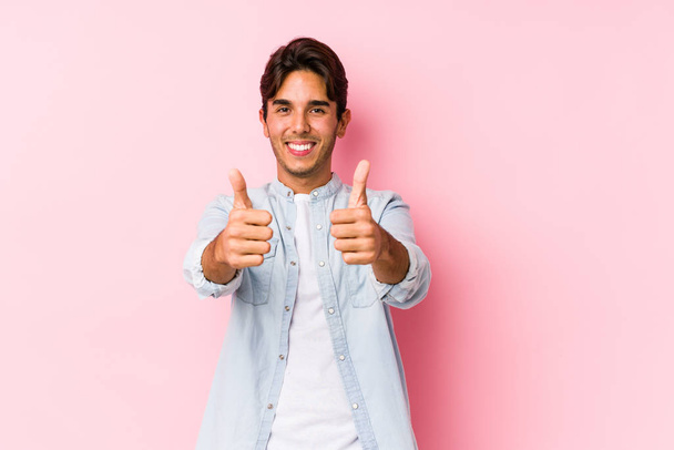 Jonge blanke man poseren in een roze achtergrond geïsoleerd met duimen ups, proost over iets, ondersteuning en respect concept. - Foto, afbeelding