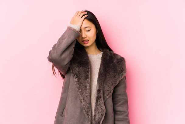 Giovane donna cinese indossa un cappotto isolato dimenticando qualcosa, schiaffeggiando la fronte con palmo e chiudendo gli occhi
. - Foto, immagini