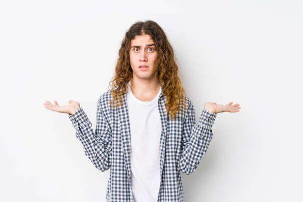 Young long hair man posing isolated confused and doubtful shrugging shoulders to hold a copy space. - Photo, Image