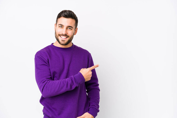 Young caucasian man against a white background isolated smiling and pointing aside, showing something at blank space. - Photo, Image
