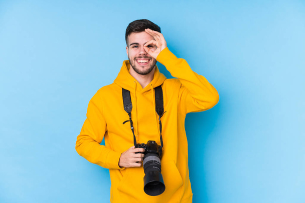 Young caucasian photographer man isolated excited keeping ok gesture on eye. - Photo, Image