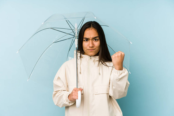 Nuori aasialainen nainen kädessään sateenvarjo osoittaa nyrkki kameraan, aggressiivinen kasvojen ilme
. - Valokuva, kuva