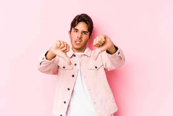 Young caucasian man posing in a pink background isolated showing thumb down and expressing dislike. - Fotografie, Obrázek