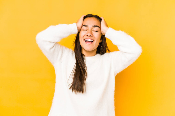 Young woman isolated on a yellow background laughs joyfully keeping hands on head. Happiness concept. - Photo, Image