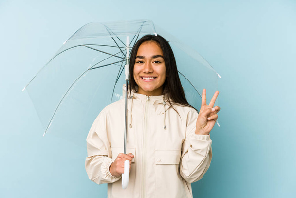 Joven mujer asiática sosteniendo un paraguas alegre y despreocupado mostrando un símbolo de paz con los dedos
. - Foto, Imagen