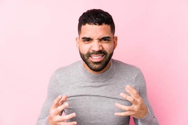 Young latin man against a pink background isolated upset screaming with tense hands. - Photo, image