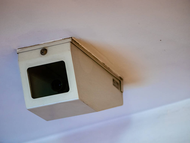 Dome κάμερα παρακολούθησης σε ένα προστατευτικό λευκό σάβανο χάλυβα με ένα διαφανές παράθυρο. Cctv βίντεο κάμερα στο λευκό ανώτατο όριο στο μετρό σε ένα κλειστό κουτί με κλειδαριά - Φωτογραφία, εικόνα