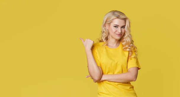 Young happy woman shows hands up, spreads his hands to the sides. Above is an empty place for text and inscription on a yellow background.  - Фото, изображение