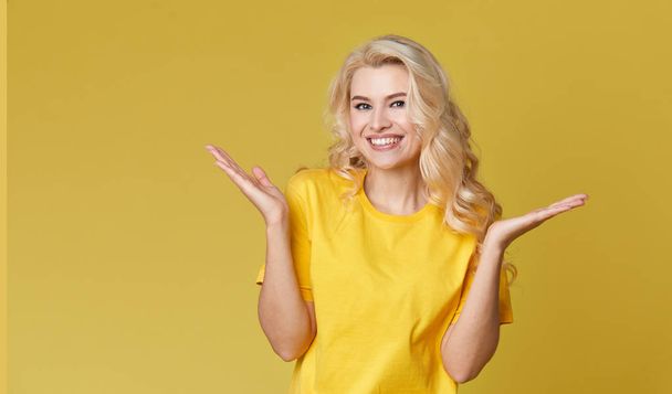 Young happy woman shows hands up, spreads his hands to the sides. Above is an empty place for text and inscription on a yellow background.  - Photo, Image