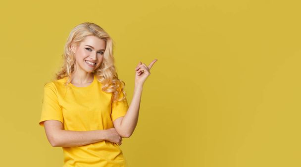 Young happy woman shows hands up, spreads his hands to the sides. Above is an empty place for text and inscription on a yellow background.  - Foto, Imagem