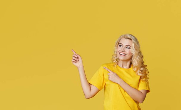 Young happy woman shows hands up, spreads his hands to the sides. Above is an empty place for text and inscription on a yellow background.  - Foto, Imagen