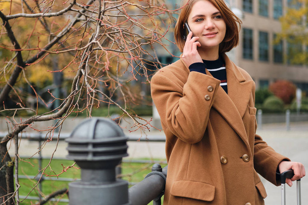 Chica bastante sonriente hablando por teléfono celular esperando sola en la calle de la ciudad
 - Foto, imagen