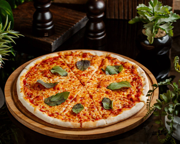 margarita pizza topped with basil leaves served on wood pizza board - Fotó, kép