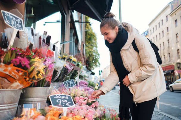 Pretty casual dziewczyna w dół kurtka szczęśliwie wybierając piękne kwiaty na ulicy miasta - Zdjęcie, obraz