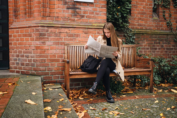 Fille décontractée attrayante avec sac à dos lecture réfléchie journal sur banc extérieur
 - Photo, image