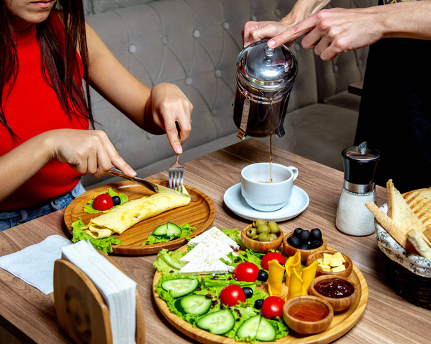 a pincér teát tölt a francia présgéptől az omlettet fogyasztó nőnek, - Fotó, kép
